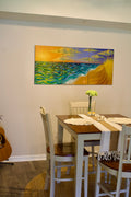 Original three-panel beach sunset painting "The Abacos" displayed above a dining table, shown with chairs, a guitar, and fresh flowers to illustrate scale in a coastal dining room.