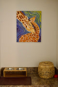 Original oil painting "Steady Ground" of a mother and baby giraffe nuzzling, with swirling blue and green brushstrokes, displayed on a wall above a pet feeding station in a cozy home nook.